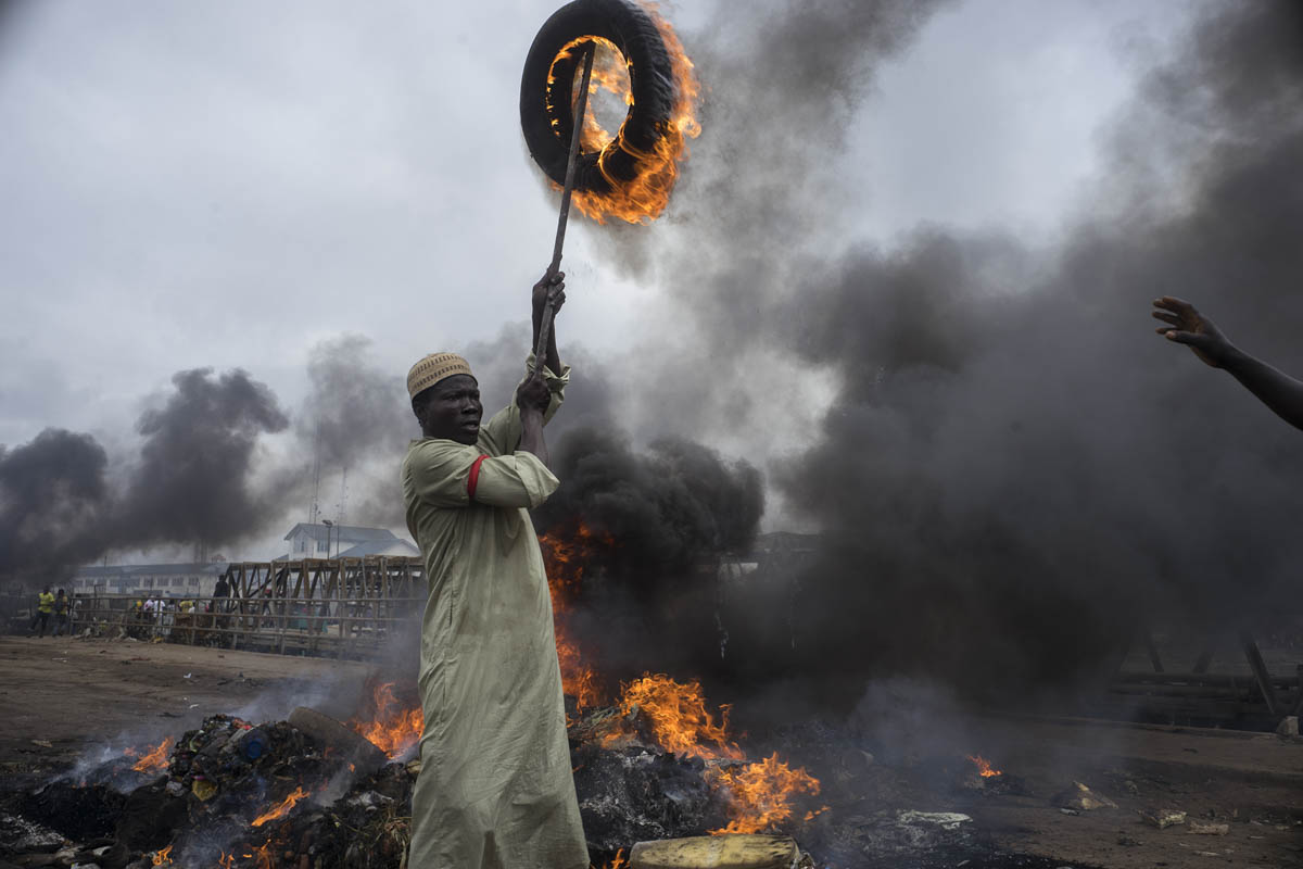 man holds aloft burning tire