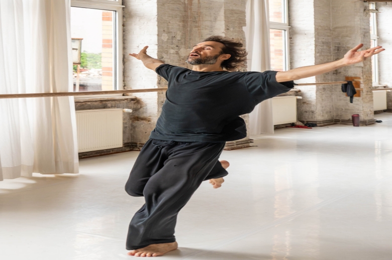 A dancer extends his arms while running during a training session in a dance studio
