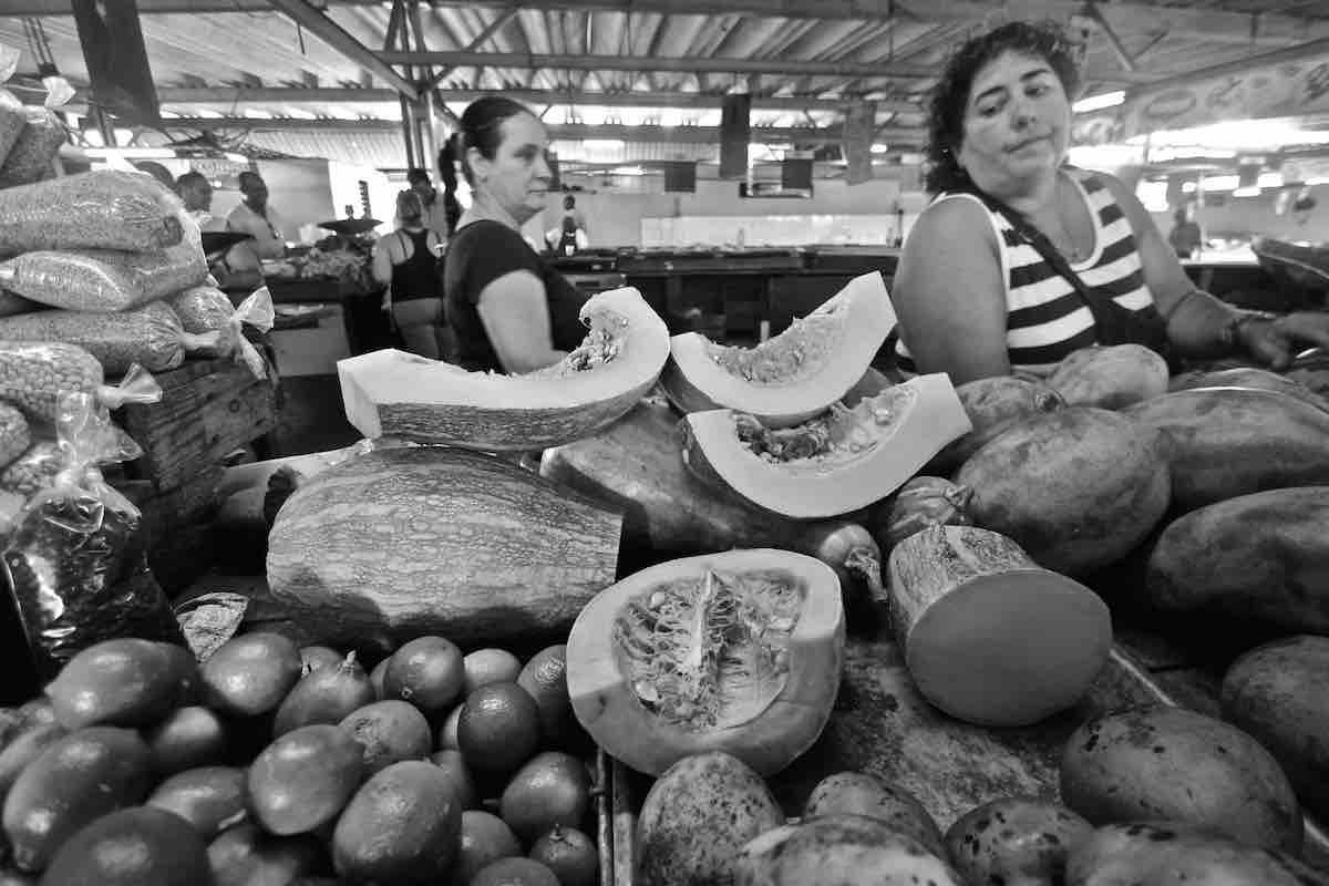 Black and white photo of a woman next to a table of produce.