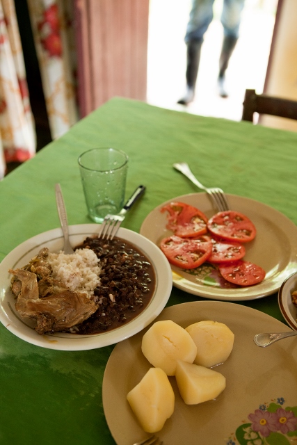 Plates of fresh sliced tomatoes, boiled potatoes, and chicken, rice, and beans. 