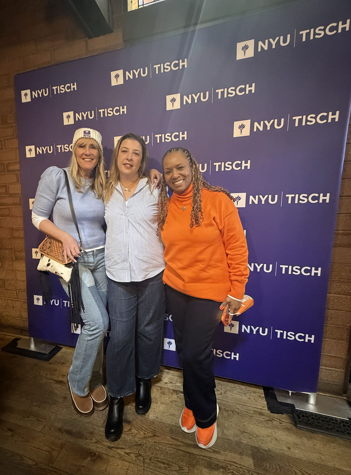 Three students standing with NYU Tisch signage/backdrop.