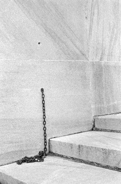 Black and white photo of a chain coming out of a wall near a flight of steps.