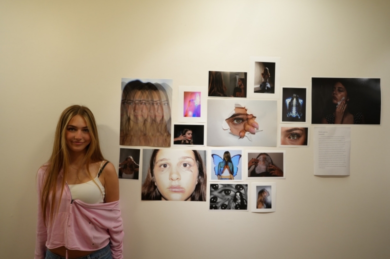 A Tisch Summer High School Photography student stands next to a display of their photography and imagery