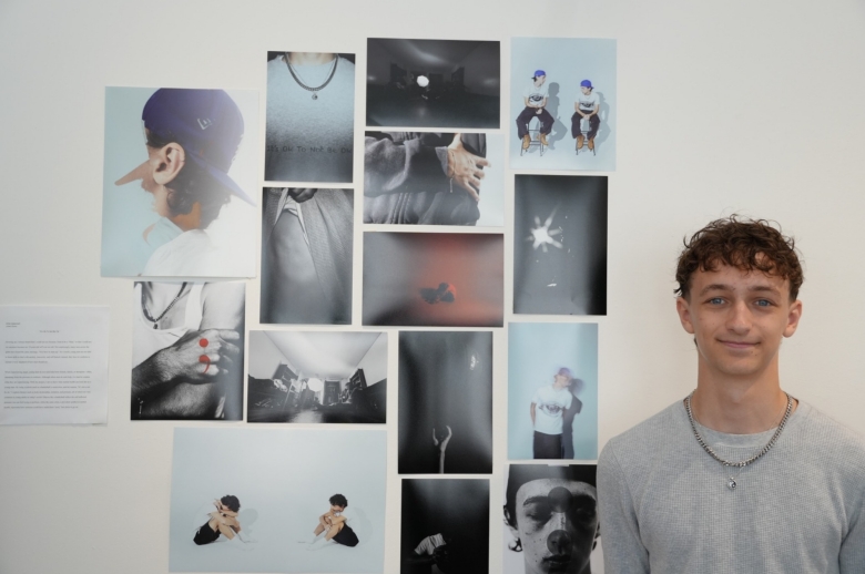 A Tisch Summer High School Photography student stands next to a display of their photography and imagery