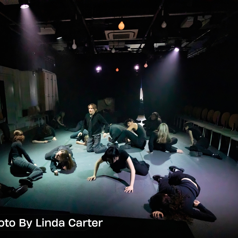 Students in various positions on the floor of a theatre with spotlights during the 2025 Shakespeare in Performance at RADA final presentation of Twelfth Night. 