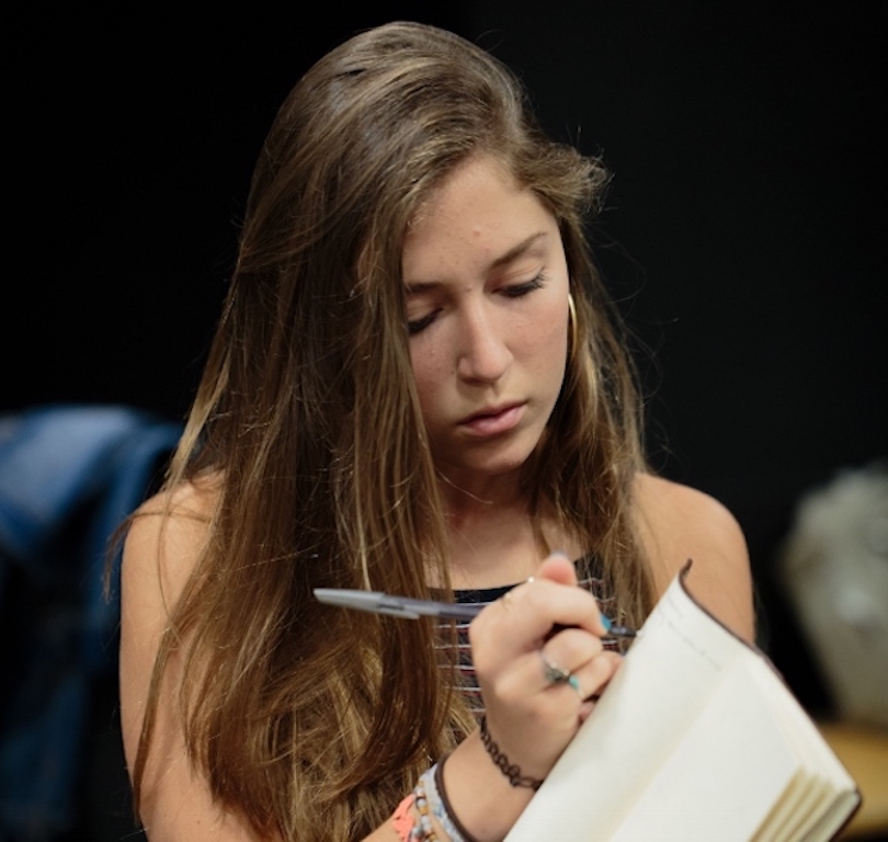 Student holding a screenplay, looking down as she writes