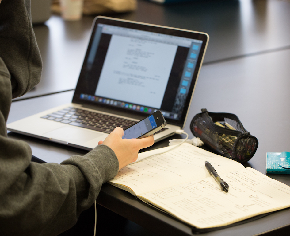 Student holding a phone and looking at a script open on a laptop computer.