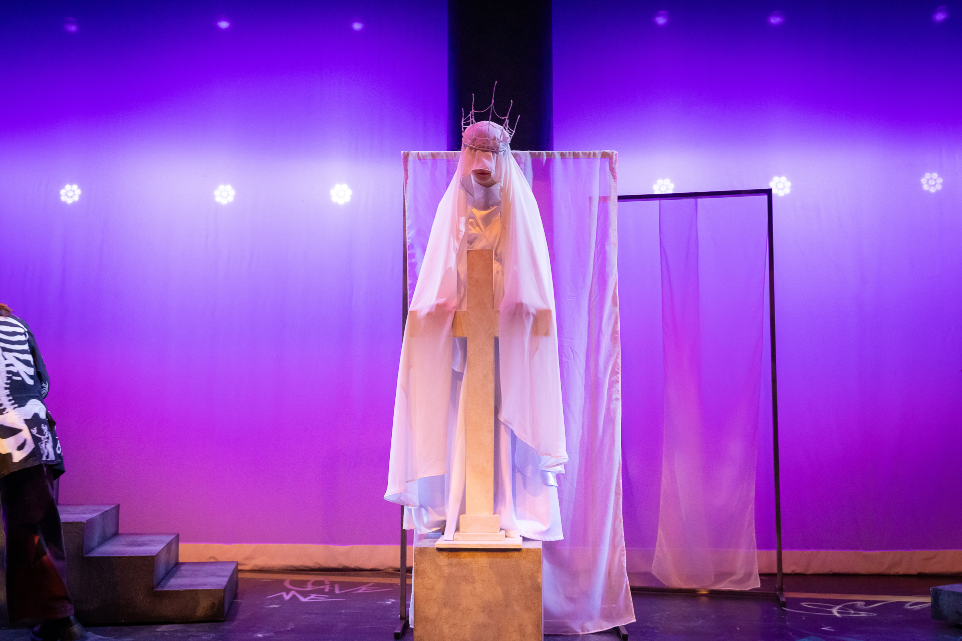 a person in long white robes standing on a box behind a large cross