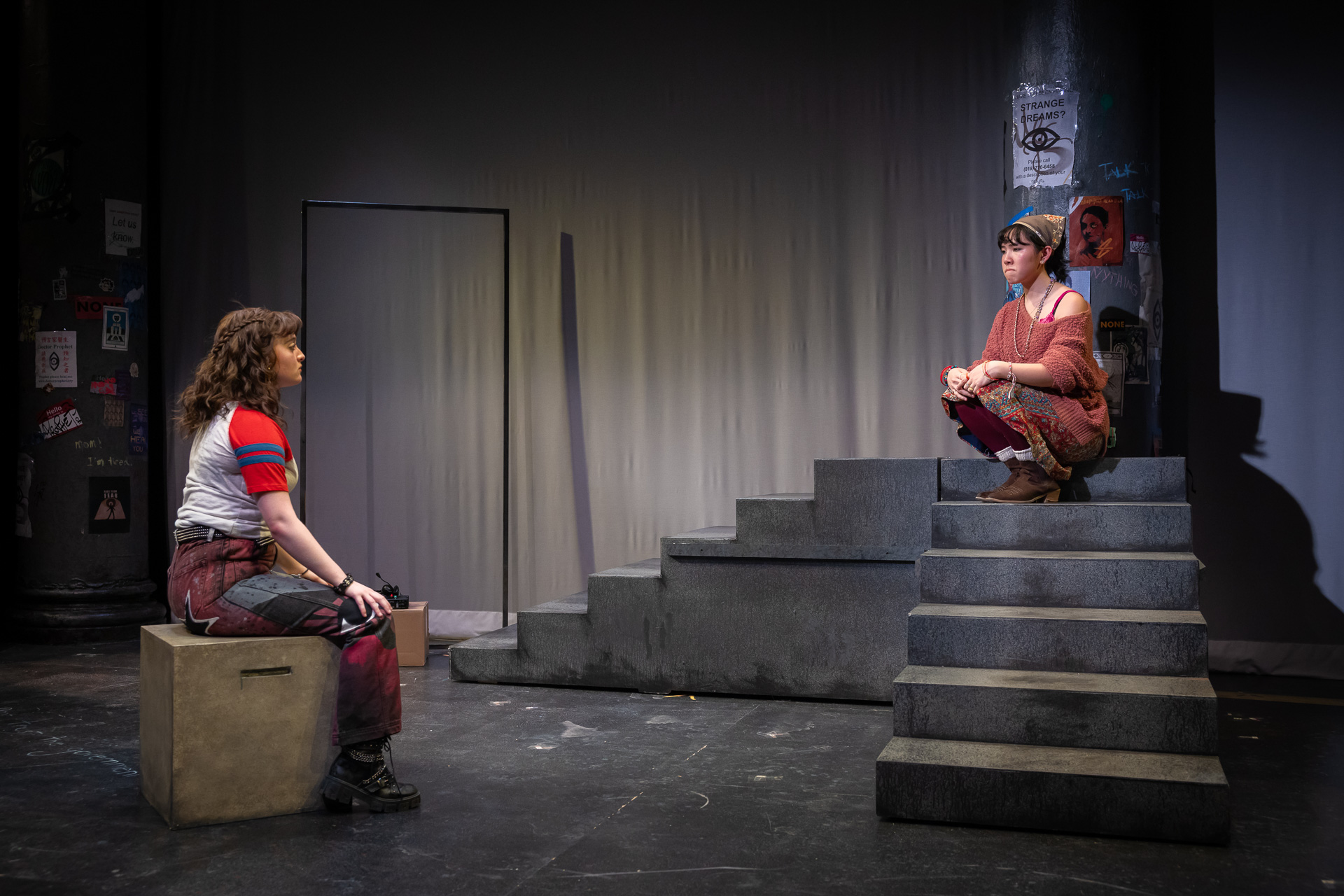 two people seated on a wooden box and a staircase looking at each other