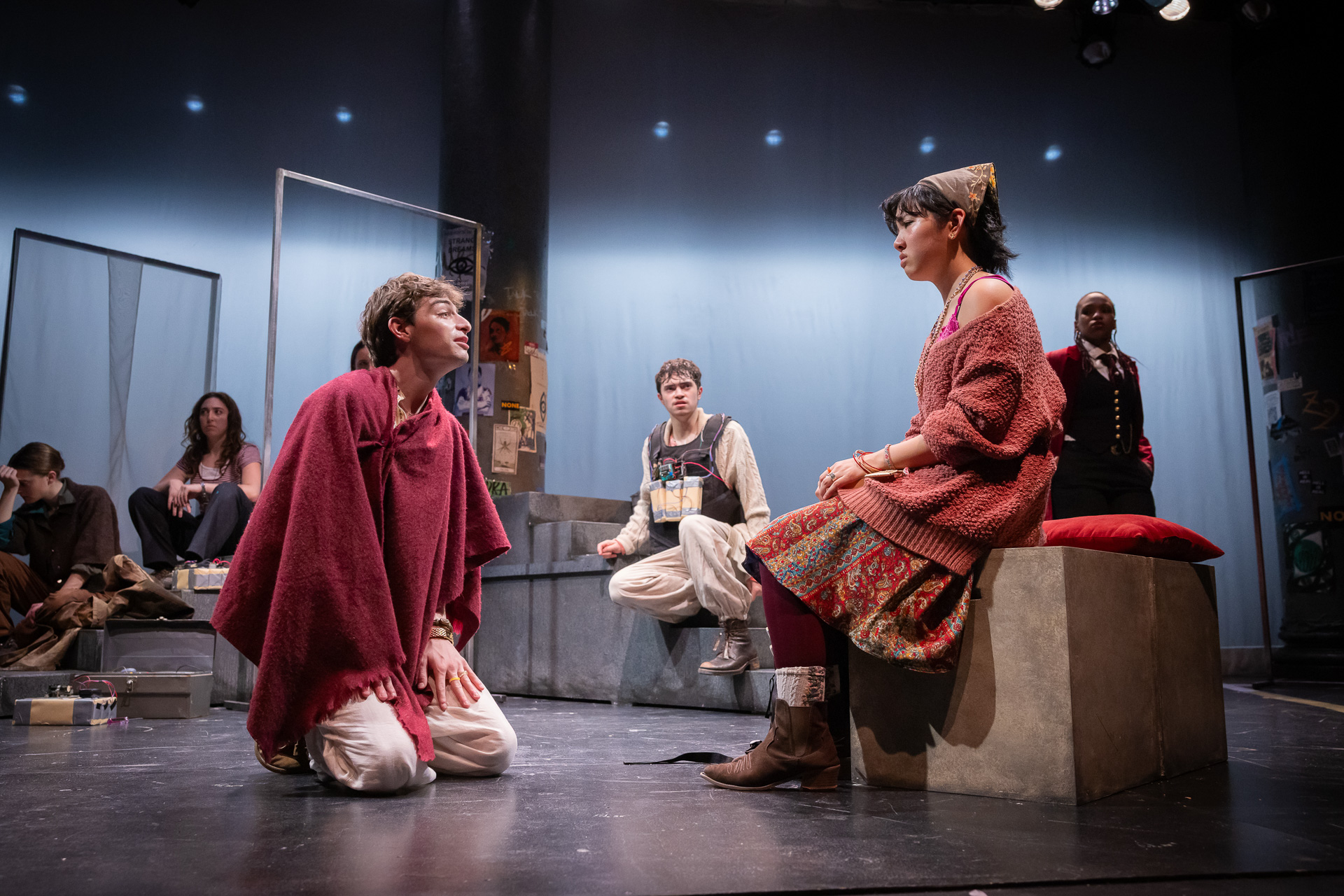 two people looking at each other on a stage with others looking on from the background