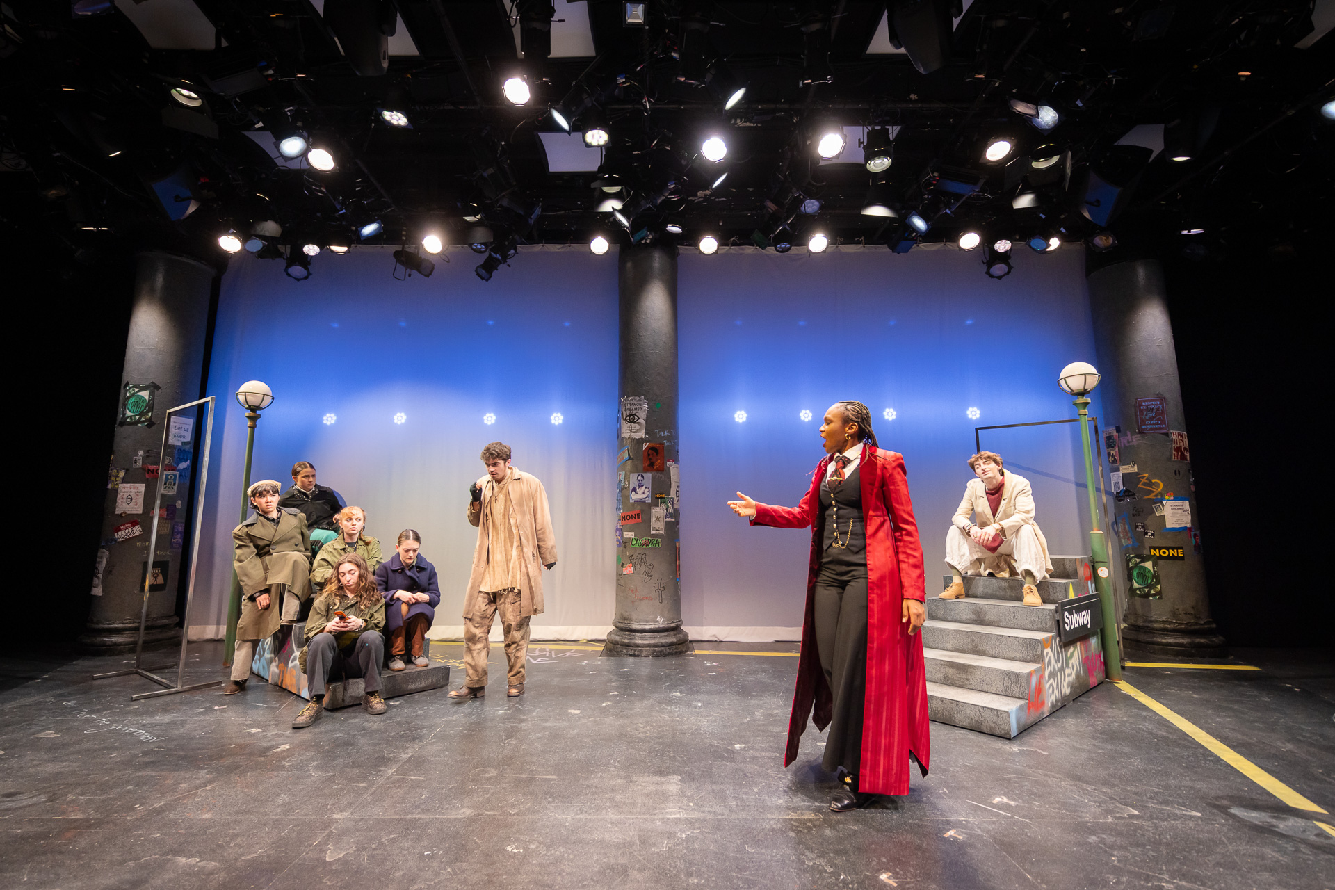 a wide shot of people on a stage, with a person in a long red coat in the foreground