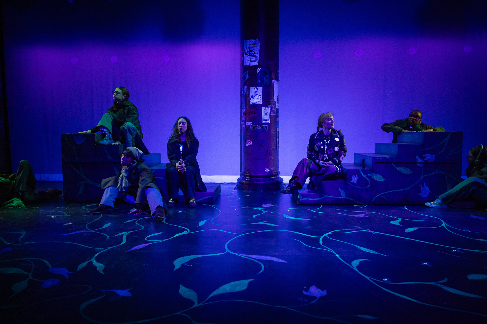 people on a dimly lit stage with a glowing floral design painted on the ground