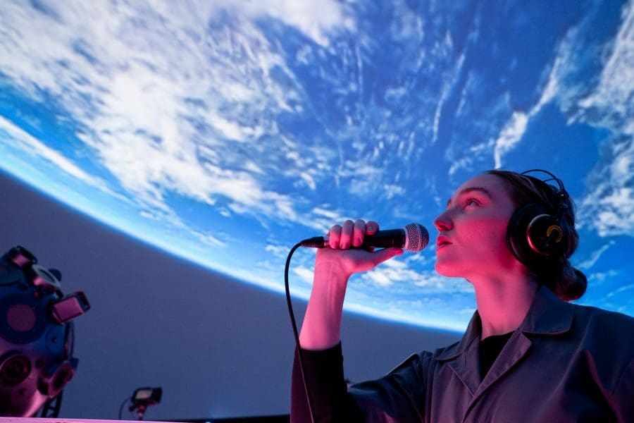Person uses headphones and microphone in front of earth projection