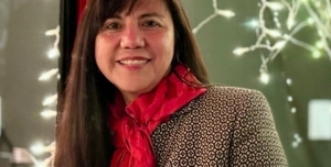 Instructor, Monica Reina wears a red scarf standing in front of led lights